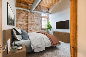 Muskegon apartment for rent - A bedroom with a brick wall and a bed with a grey comforter.