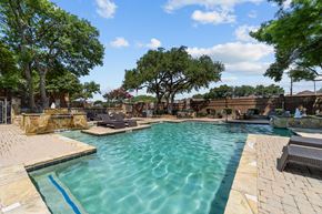 Dallas apartment for rent - A large outdoor swimming pool surrounded by trees and lounge chairs.