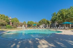 Denton apartment for rent - a swimming pool with umbrellas and buildings in the background at Fountains of Denton in Denton, TX