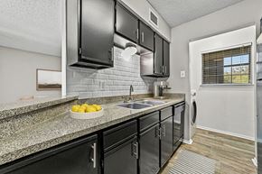 Plano apartment for rent - a kitchen with black cabinets and a counter top with a sink at Legacy Apartments in Plano, TX