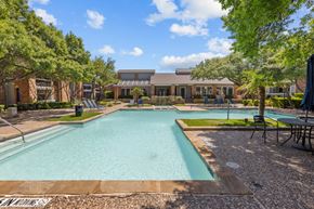 Dallas apartment for rent - A large outdoor swimming pool surrounded by trees and a building in the background.