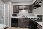 Dallas apartment for rent - A kitchen with brown cabinets and black appliances.