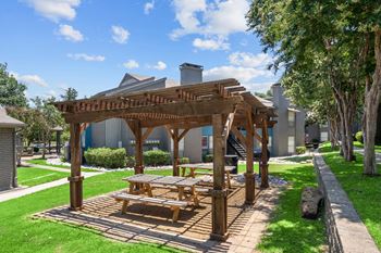 A wooden pergola with a picnic table in the middle of a grassy area