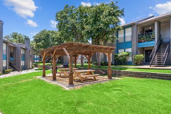 A wooden gazebo with a picnic table in the middle of a grassy area