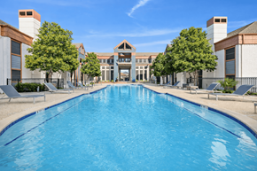 Dallas apartment for rent - A large swimming pool in front of a building with trees on the side.