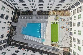 Kyle apartment for rent - A swimming pool is surrounded by a grassy area and concrete walkways. at ThreeTwenty at the Vybe Apartments, Kyle, 78640
