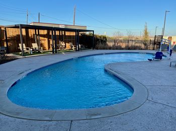A large outdoor swimming pool with a curved edge and a concrete patio surrounding it.