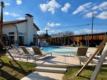 A pool area with sun loungers and a building in the background.