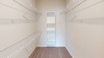 A walk-in closet with a carpeted floor and white shelving.