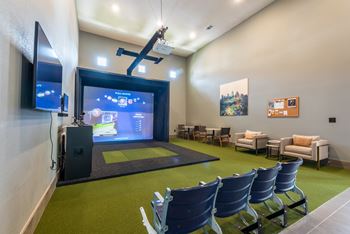 A room with green carpet and chairs and a large screen on the wall