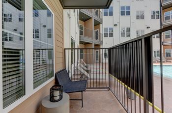 A balcony with a black chair and a lantern on a table.