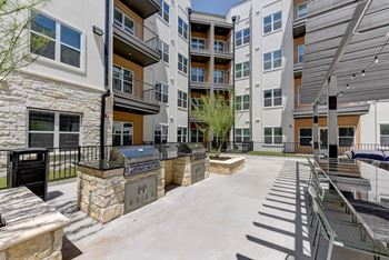 A courtyard with a grill and a bench is surrounded by apartment buildings.