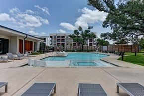 Austin apartment for rent - A swimming pool surrounded by lounge chairs and trees.