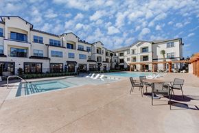 Austin apartment for rent - A large outdoor swimming pool surrounded by chairs and buildings at Bridge at Speyside Apartments, Texas
