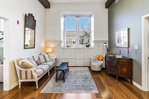 Baltimore apartment for rent - A living room with a white couch, a black coffee table, and a window with a view of a tree.