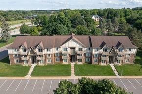 Lake Orion apartment for rent - A large, multi-story building with a brown roof and white walls, surrounded by a grassy lawn and trees.