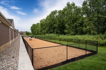 A tennis court is surrounded by a black fence and a gravel path