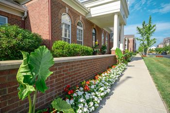 A brick building with a white porch and a flower bed in front