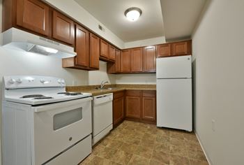 A kitchen with white appliances and wooden cabinets and a white refrigerator
