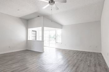 An empty living room with white walls and a ceiling fan