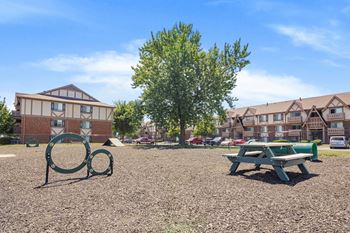 A playground with a green bench and a tree in the foreground and apartment buildings in the background