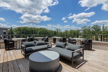 A wooden deck with grey couches and tables.