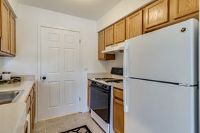 Macomb apartment for rent - A white refrigerator stands in a kitchen with wooden cabinets and a white doors  at Northport Apartments, Macomb, MI, 48044