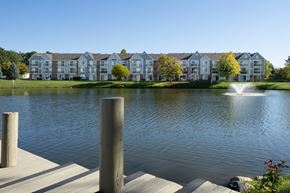 Westland apartment for rent - A lake in front of apartment buildings with a fountain in the middle at The Landings Apartments, Westland