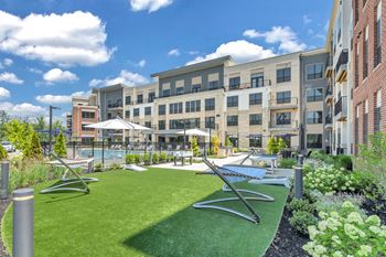 A sunny day at a modern apartment complex with a green lawn and a pool.