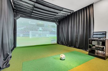 A soccer ball is on a green mat in front of a screen showing a soccer game.