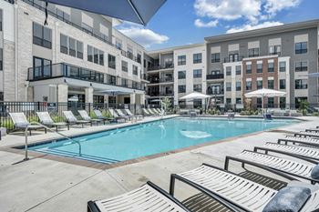 A swimming pool surrounded by sun loungers and umbrellas in front of apartment buildings