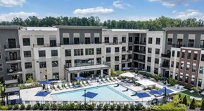 Midlothian apartment for rent - A large swimming pool surrounded by a fence and umbrellas in front of apartment buildings at Luxe 360 Apartment Complex in Midlothian Virginia
