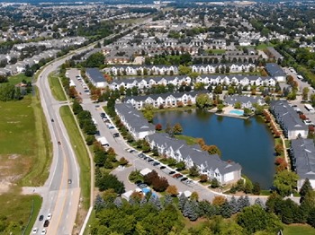 An aerial view of a subdivision with a lake and cars parked on the side of the road