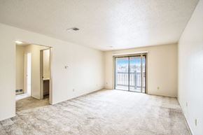 Kalamazoo apartment for rent - A spacious living room with a carpeted floor and a sliding glass door leading to a balcony at Seville Apartments, Kalamazoo, MI