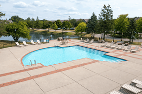 Wixom apartment for rent - A large outdoor swimming pool surrounded by lounge chairs and trees.