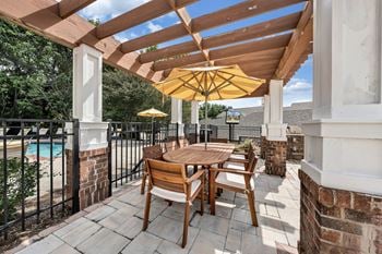 A wooden table and chairs are set up on a patio with a yellow umbrella.