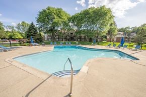 Lake Orion apartment for rent - A large swimming pool surrounded by trees and lounge chairs.