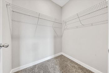 Empty walk-in closet with wire shelves and carpeted floor.