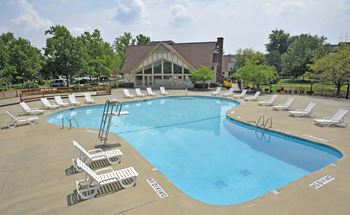 A swimming pool with chaise lounge chairs and a club house in the background