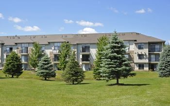 An apartment building on a grassy hill with trees in front of it