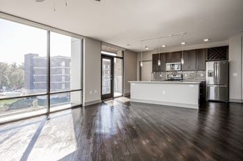 An empty living room with a kitchen and a large window