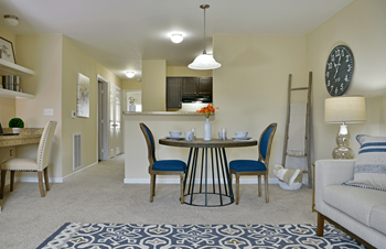 A dining area with a table and chairs and a kitchen in the background