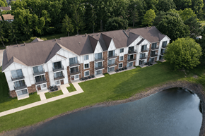 Novi apartment for rent - A large building with a brown roof is surrounded by a grassy area and a body of water.