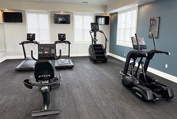 A spacious gym with treadmills, elliptical machines, and a television