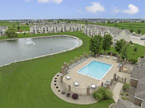 Champaign apartment for rent - A large swimming pool surrounded by a grassy area and a pond at Hunters Pond Apartment Homes, Illinois