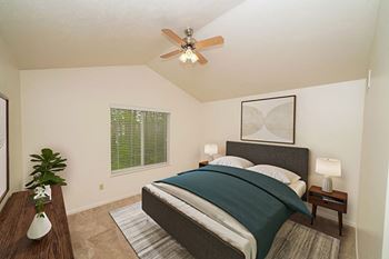 A bedroom with a bed, nightstand, and a cathedral ceiling with ceiling fan in townhome master bedroom