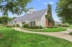 Portage apartment for rent - A community building with a grey roof and a chimney is surrounded by green grass and trees at Newport Village Apartments, Portage, 49002