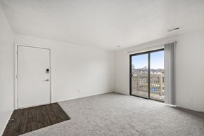 Michigan City apartment for rent - A living room with plush carpet and a slider to a private balcony with a view at Normandy Village Apartments, Michigan City, 46360