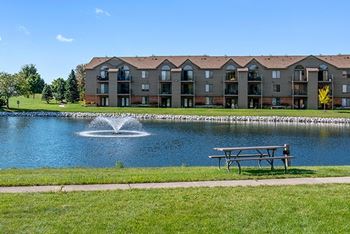 A large building with a pond, fountain and picnic table behind it 