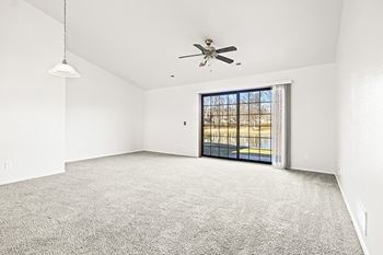 A spacious living room with a ceiling fan and a sliding glass door leading to a patio